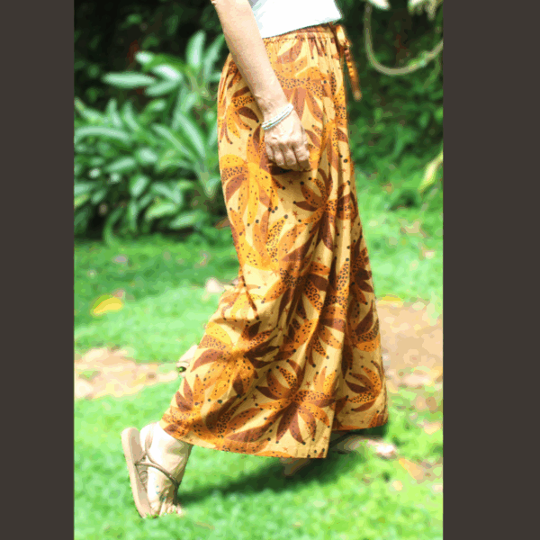 Femme en mouvement portant le pantalon fluide en lin imprimé tropical et aux tons chauds, soulignant la liberté de mouvement et le tombé élégant du vêtement confortable."
